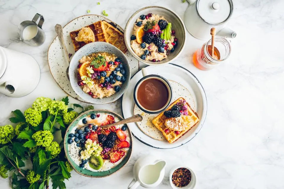 Table de petit-déjeuner vue de dessus : bols de fruits rouges, yaourt, gaufres et légumes verts
